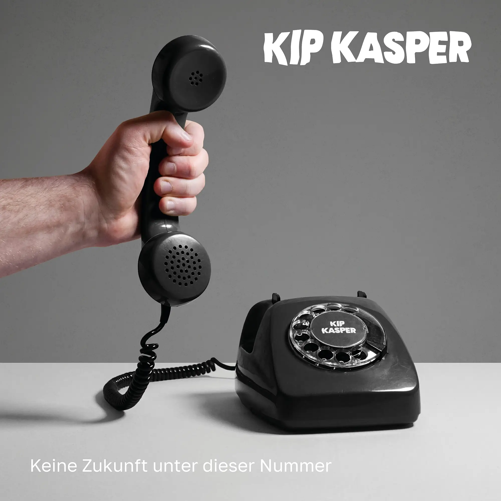An old phone on the table is picked up by a male hand in front of a grey background. Album cover for KIP KASPER.